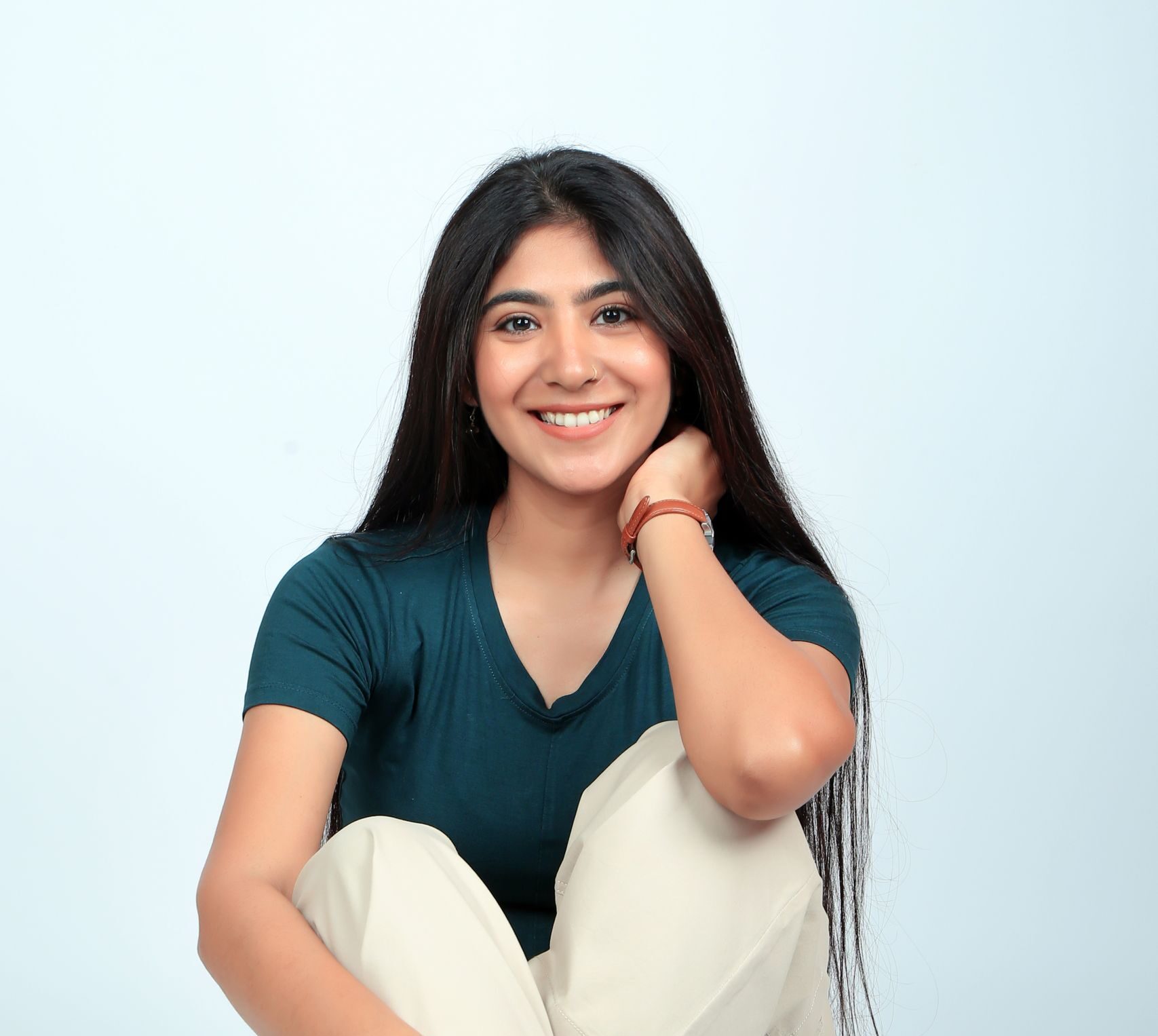 Portrait of a smiling woman in casual attire sitting on a studio floor.